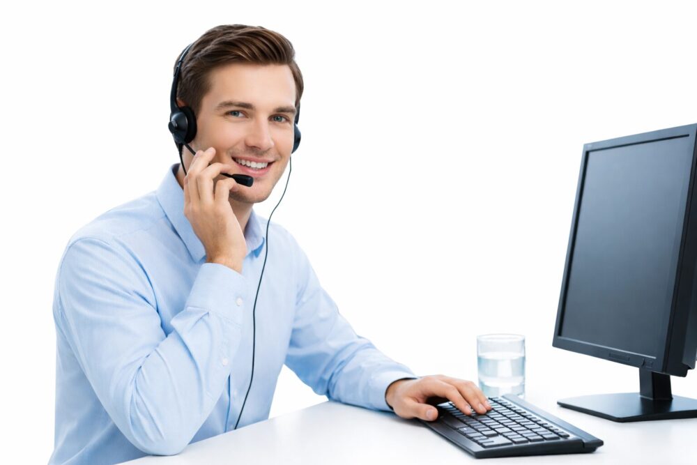 Smiling customer service agent wearing a headset and working at a computer in a modern office